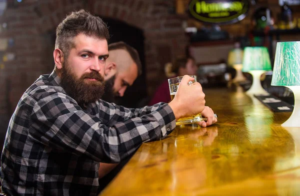 Brutal hipster bearded man sit at bar counter drink beer. Order alcohol drink. Bar is relaxing place have drink and relax. Hipster relaxing at bar with beer. Man with beard spend leisure in dark bar