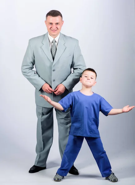 Dad boss. Father and cute small son. Child care development upbringing. Respectable profession. Family business. Man respectable businessman and little kid doctor uniform. Doctor respectable career