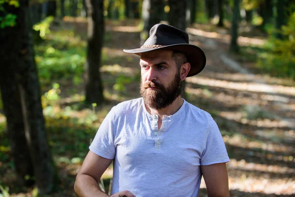 Vaquero valiente. camping y senderismo. macho maduro con mirada brutal. Hombre barbudo con sombrero de vaquero caminar en el parque al aire libre. hombre hipster relajarse en el bosque de otoño. Primavera tiempo soleado. Vaquero serio y confiado —  Fotos de Stock