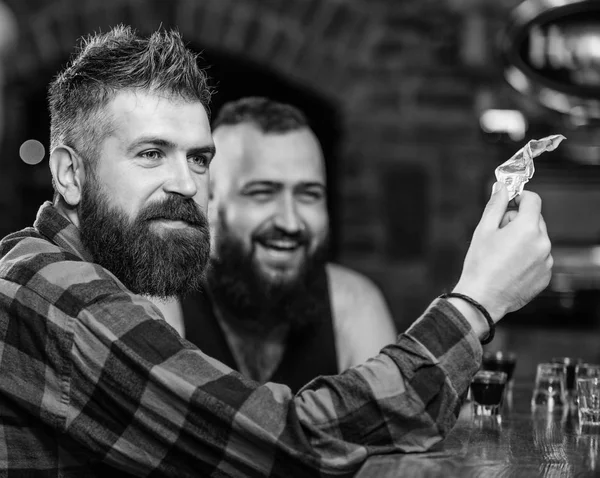 Жестокий бородатый хипстер проводит время с другом за барной стойкой. Мужчины отдыхают в баре. Дружба и досуг. Пятница отдых в баре. Друзья отдыхают в пабе. Заказать напитки в баре — стоковое фото
