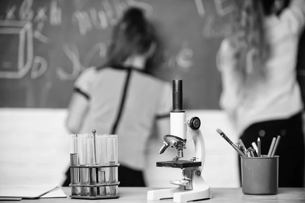 Schüler an der Tafel im Chemieunterricht. pädagogisches Experimentierkonzept. Mitschülerinnen studieren Chemie. Mikroskop und Reagenzgläser auf dem Tisch. Chemische Reaktionen. Chemie-Studium interessant machen — Stockfoto