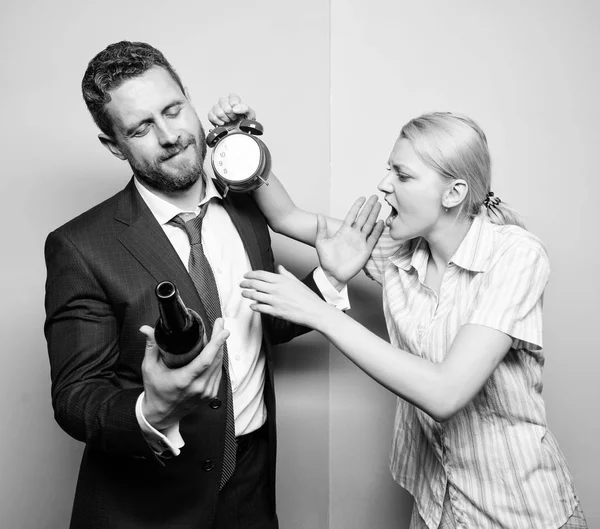 Caught for coming home late. Man suffering from alcoholism. Angry wife meeting drunk husband late at home. Businessman with alcohol bottle and woman with clock. Addictive alcoholism or alcohol abuse