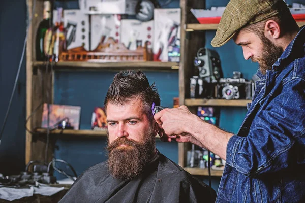 Barbiere con taglierina che taglia capelli su tempio di cliente. Concetto di stile di vita hipster. Un cliente hipster che si taglia i capelli. Barbiere con tagliacapelli lavora su acconciatura per barbuto uomo barbiere sfondo — Foto Stock