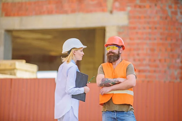 Construction project inspecting. Safety inspector concept. Construction site safety inspection. Discuss progress project. Woman inspector and bearded brutal builder discuss construction progress