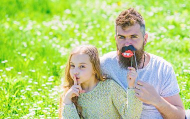 Aile açık havada eğlence harcamak. Çocuk sessizlik jest gösterirken booth öznitelik fotoğraf çocuk ve babası dudakları ile poz. Gizli kavramı. Baba ve kızı oturur, grassplot, arka planı yeşil çimenlerin üzerinde