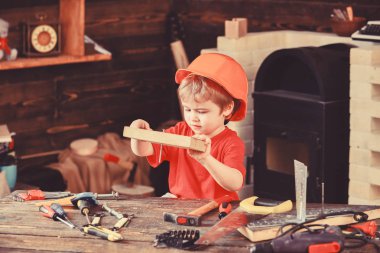 Miğferli şirin çocuk inşaatçı ya da tamirci olarak oynuyor, tamir ediyor ya da el işi yapıyor. El işi konsepti. Meşgul suratlı çocuk atölyede evde oynuyor. Çocuk tahtaya çivi çaktı.