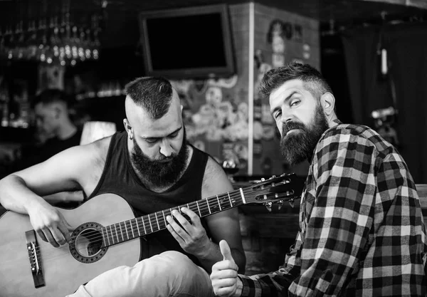 Live music concert. Acoustic performance in pub. Hipster brutal bearded with friend in pub. Cheerful friends sing song guitar music. Relaxation in pub. Friends relaxing in pub. Man play guitar in pub