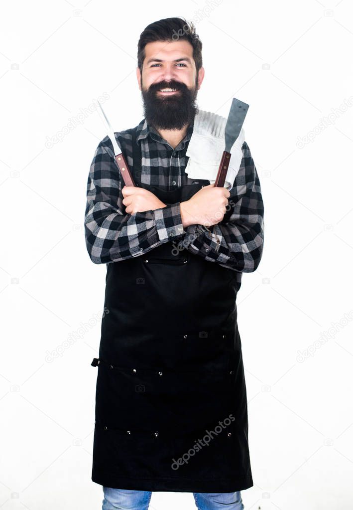 Using a barbecue set. Confident grill cook. Bearded man holding grill gripper tools. Hipster in apron with metal utensils for barbecue grill. Preparing food on grill