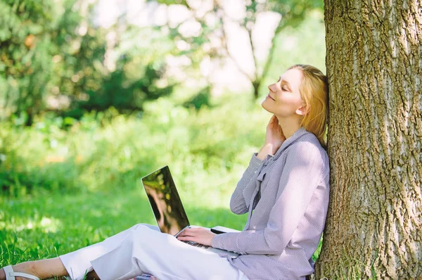 Женщина с ноутбуком работает на открытом воздухе постное дерево. Минута отдыха. Образовательные технологии и интернет-концепция. Девушка, работающая с ноутбуком в парке, сидит на траве. Природный офис. Преимущества работы на открытом воздухе — стоковое фото