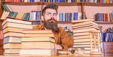 Kitap kurdu kavramı. Öğretmen ya da öğrenci sakallı kum saati ve gözlük, defocused ile masaya otur. Katı yüz sit Kitaplığı'nda, eğitim sırasında kitaplar, kitap rafı arka plan üzerinde yığınları arasında adam