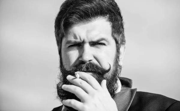 Les cigarettes nous aident dans tout, de l'ennui à la maîtrise de la colère. Un homme avec une moustache barbe tient une cigarette. Barbu hipster fumer cigarette ciel arrière-plan. Guy cigarette profiter influence de la nicotine — Photo