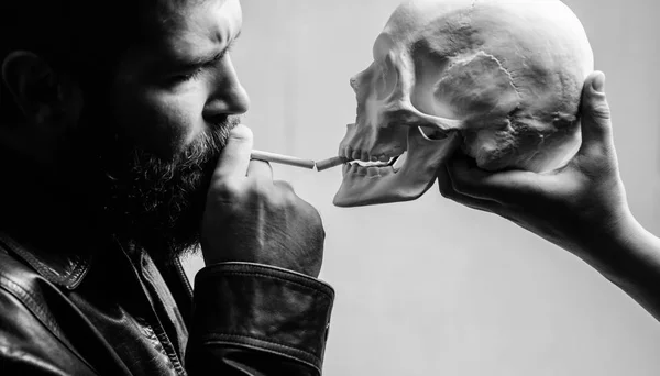 Habit to smoke tobacco bring harm to your body. Man smoking cigarette near human skull symbol of death. Harmful habits. Smoking cause health damage and death. Destroy your health. Smoking is harmful