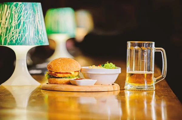 High calorie snack. Hamburger and french fries and tomato sauce on wooden board. Delicious burger. Burger with cheese meat and salad. Pub food and mug of beer. Fast food concept. Burger menu