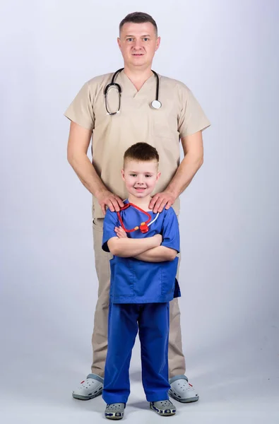 Rapazinho com o pai no hospital. pai e filho de uniforme médico. criança feliz com pai com estetoscópio. médico de família. medicina e saúde. Outro dia de trabalho. equipe hospitalar de médicos — Fotografia de Stock