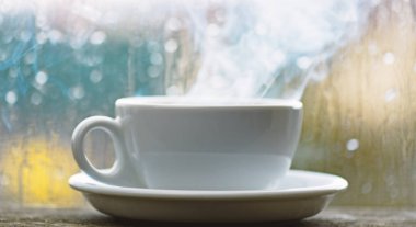 Kahve yağmurlu günde zevk. Taze yapılmış kahve beyaz fincan veya kupa pencere üzerinde. Yağmurlu bir gün kahve zamanında. Islak cam pencere ve sıcak kahve. Sonbahar bulutlu hava kafein içecek ile daha iyi