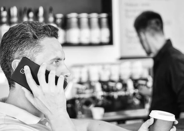 Man holds cup of drink while have mobile conversation. Coffee to go useful option for busy people. Call friend to have drink together. Guy busy speak phone while relax coffee break. Ready to hear you