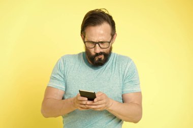 Gözlüklü adam kafası karışmış, akıllı telefon kullanıyor. İnsan kullanıcısı uygulama akıllı telefonuyla etkileşim kurar. Sakallı, olgun etkileşimli mobil arayüz uygulaması. Olgun insanlar için dijital cihazlara alışmak zor.