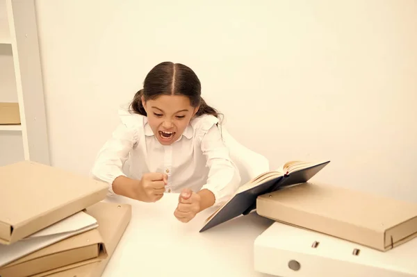 Pilně studuješ. Dívka dítě čte knihu zatímco sit tabulky bílé pozadí. Školačka studium a čtení knih. Kid školní uniforma rozzlobený podrážděné obtížný úkol. Emocionální podrážděný výraz žáka — Stock fotografie