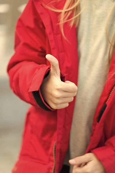 Hand of baby shows thumbs up gesture. Kid wear warm jacket show gesture of approvement or accept. She likes this. Thumb up gesture meaning like and agreement. Thumbs up and like concept