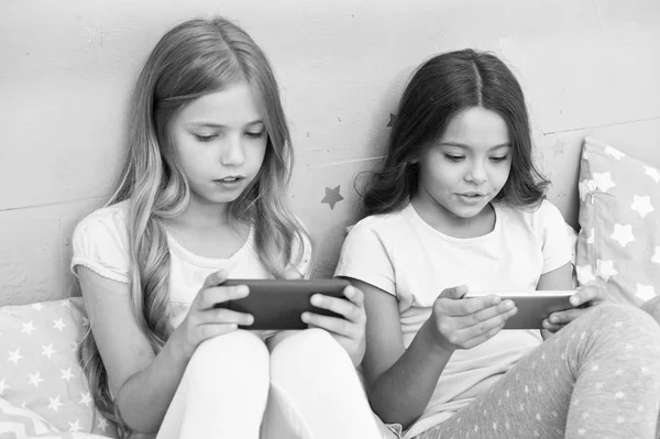 Children in pajama interact with smartphones. Application for kids fun. Internet surfing and absence parental advisory. Smartphone internet access. Girls sisters wear pajama busy with smartphones