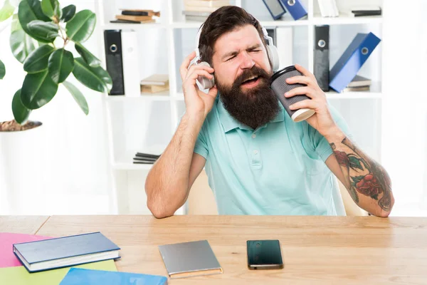 常规办公日。男子胡子的家伙耳机坐在办公室听音乐唱歌。带咖啡杯的工人开始工作日与最喜欢的歌曲。灵感和充满活力。办公室生活节奏 — 图库照片