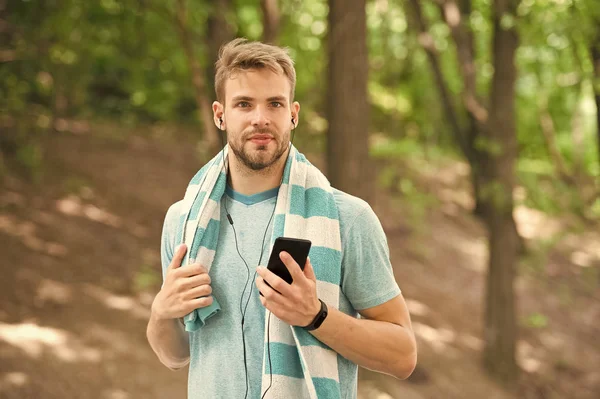 Mi godo la musica dopo una bella corsa. Atleta uomo che crea playlist musicale con app per smartphone, sfondo naturale. Addestramento sportivo con gadget musicale. Atleta con fitness tracker musica d'ascolto — Foto Stock