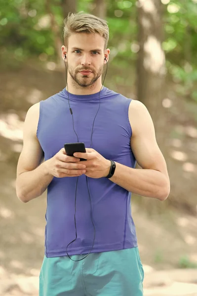 Music best companion to run. Man athlete on busy face set up play list, nature background. Sportsman training headphones listen music. Proper play list helps sportsman run or training better