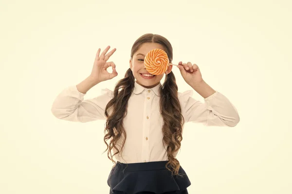 Menina cara feliz detém doce pirulito ok gesto. Alimentação do almoço escolar. A rapariga gosta de doces brancos isolados. Estudante recompensado com doces por excelentes notas. Realização escolar e recompensa doce — Fotografia de Stock