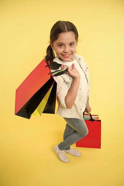 Gelukkig kind houden boodschappentassen op gele achtergrond. Kleine shopaholic glimlach met papieren tassen. Meisjesshopper bereidt zich voor op verjaardag, mode. Zwart vrijdagconcept. Veel plezier met winkelen. Grote verkoop — Stockfoto