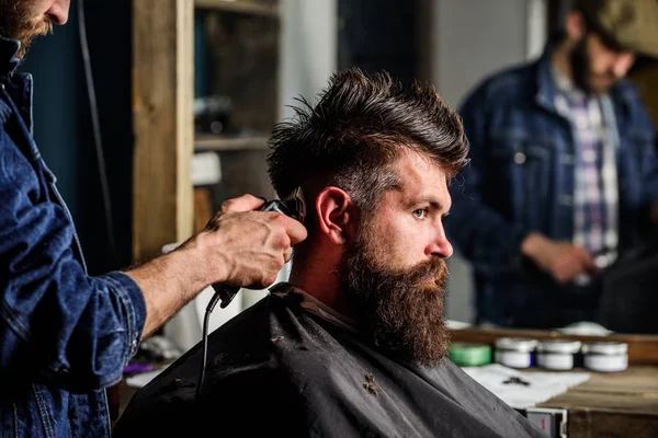 Barber styling hair of brutal bearded client with clipper. Barber with hair clipper works on hairstyle for bearded man barbershop background. Hipster lifestyle concept. Hipster client getting haircut — Stock Photo, Image