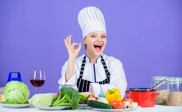 Woman chef wear hat apron near table ingredients. Girl adorable chef teach culinary. Best culinary recipes to try at home. Perfect recipe. Turn ingredients into delicious meal. Culinary skills