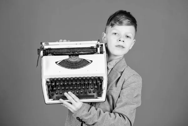 Usando tecnología retro. Niño sosteniendo una máquina de escribir retro sobre fondo azul. Un niño pequeño con una vieja máquina de escribir. Niño inteligente con máquina de escribir vintage. Lindo chico con máquina de escribir mecánica de escritorio — Foto de Stock