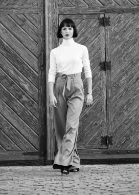 Şık kıyafet ince uzun Bayan. Kadın güvenle yürümek. Kadın moda esmer açık havada ahşap arka plan ayakta. Moda ve stil kavramı. Kız makyaj moda giysiler içinde poz ile