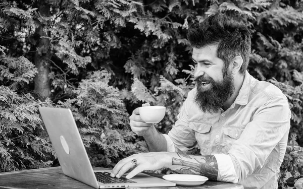 Um programador de computador freelancer. Homem barbudo a trabalhar por conta própria. Freelancer desfrutar de café e Wi-Fi gratuito. Freelance profissional trabalhando fora do local. Hipster fazendo trabalho freelance no computador portátil — Fotografia de Stock
