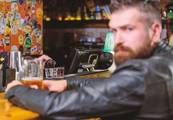 Brutal hipster bearded man sit at bar counter drink beer. Friday evening. Bar is relaxing place to have drink and relax. Man with beard spend leisure in dark bar. Hipster relaxing at bar with beer