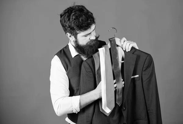 Shopping concept. Shop assistant or personal stylist service. Stylist advice. Matching necktie with outfit. Man bearded hipster hold neckties and formal suit. Guy choosing necktie. Perfect necktie