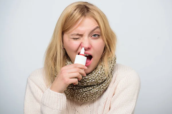 Clearing up. Sick woman spraying medication into nose. Unhealthy girl with runny nose using nasal spray. Cute woman nursing nasal cold or allergy. Treating common cold or allergic rhinitis