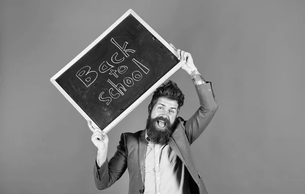 Teacher with tousled hair cheerful about school year beginning. Keep working and be kind to people. Stay positive. Teacher bearded man holds blackboard with inscription back to school blue background