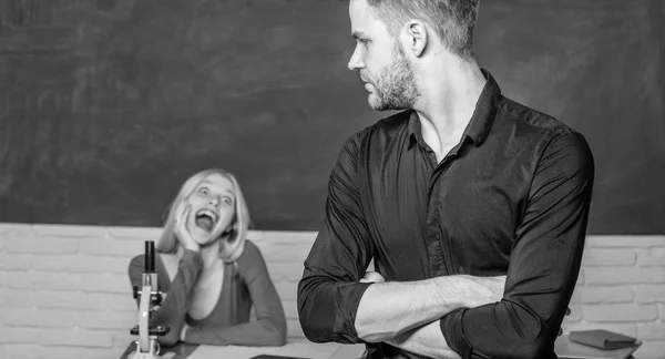 Svarande hem uppdraget. Manlig student med examinator vid undersökningen. Stilig man stående händerna korsade i klassrummet med lärare. High school student säger lektion. Universitet eller college student — Stockfoto