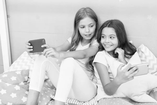 Internet surfing and absence parental advisory. Smartphone internet access. Girls sisters wear pajama busy with smartphones. Children in pajama interact with smartphones. Application for kids fun