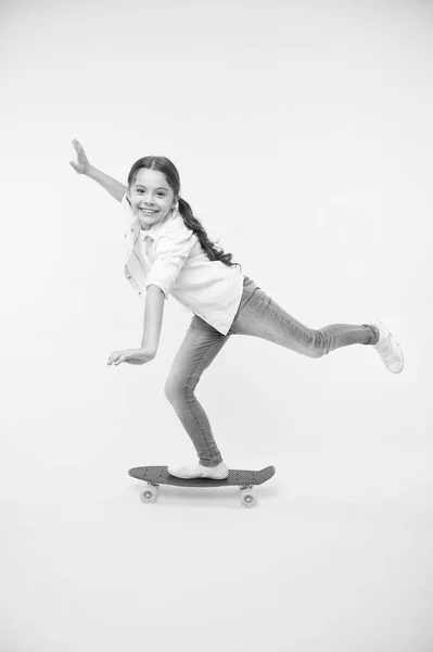 子供ペニー ボードを楽しんでいます。趣味好きな活動。子供の笑顔はスケート ボードの上に立ちます。ペニーは、女の子のためのかわいいカラフルなスケート ボードをボードします。乗ることができます。女の子に乗るペニー ボード黄色背景 — ストック写真