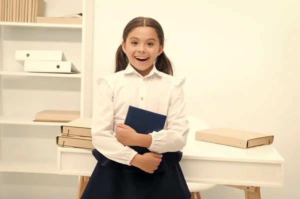 Рад вступить в первый класс. Девочка держит книжный столик на белом фоне. Школьнице нравится учиться и посещать уроки. Детская школьная форма улыбающееся лицо любит посещать школьные уроки — стоковое фото