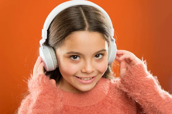 Niña linda niña usar auriculares escuchar música. Niño escuchar música fondo naranja. Música recomendada basada en el interés inicial. Dime lo que escuchas, y te diré quién eres — Foto de Stock