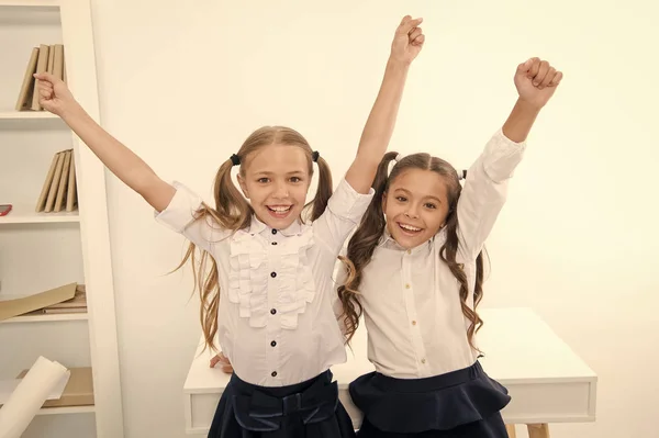 Gelukkige leerlingen houden elkaars handen omhoog in het klaslokaal, overwinningsconcept. Kleine meisjes vieren de overwinning. Wij zijn de winnaars. gelukkig kleine meisjes. — Stockfoto