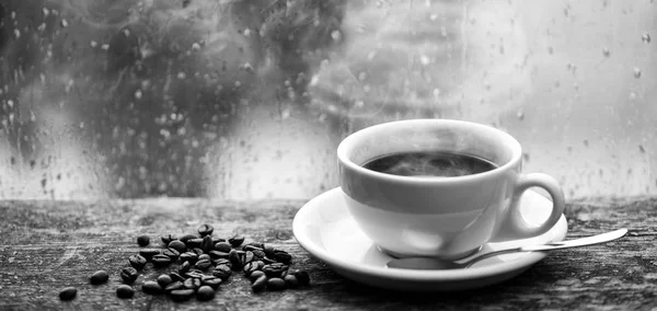 Наслаждаюсь кофе в дождливый день. Кофейный утренний ритуал. Свежий кофе белая кружка и бобы на подоконнике. Мокрое стекло и чашка горячего кофе. Осенняя облачная погода лучше с кофеином — стоковое фото