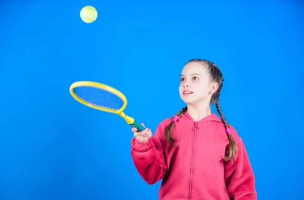 女の子愛らしい子供はテニスをプレイ。テニスのスキルを練習し、楽しみを持っています。青い背景にアスリートの子供のテニスラケット。アクティブなレジャーと趣味。テニススポーツとエンターテイメント。ボールに焦点を当てた — ストック写真