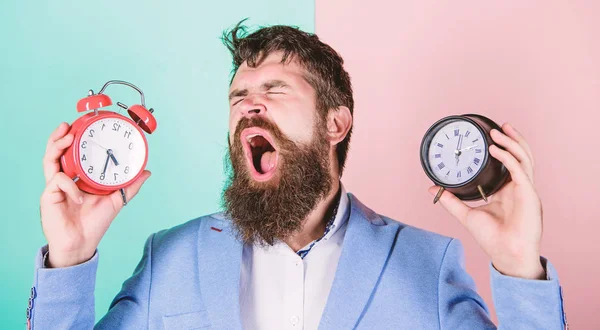 Guy unshaven puzzled face having problems with changing time. Time zone. Changing time zones affect health. Does changing clock mess with your health. Man bearded hipster hold two different clocks