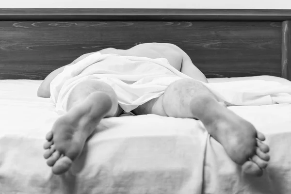 Feet of man sleeping in comfortable bed. A young man waking up in bed and stretching his arms. Man on bed.