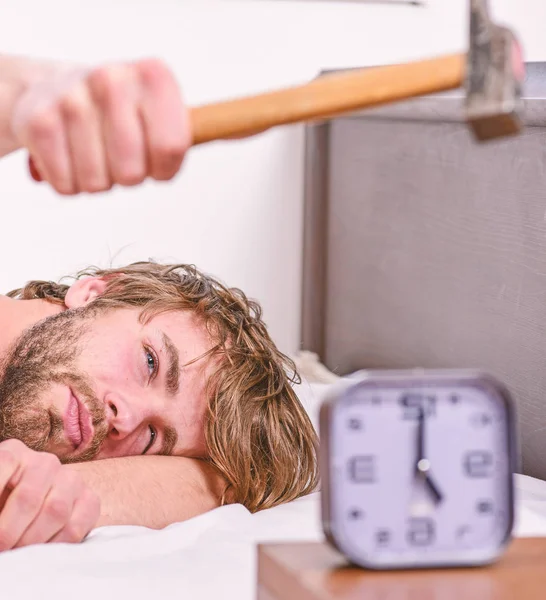 Un tipo tocando con un martillo sonando el despertador. Romper el régimen de disciplina. Un sonido molesto. Hombre barbudo molesto cara somnolienta yacía almohada cerca del despertador. Deja de sonar. Molesto despertador sonando —  Fotos de Stock