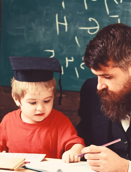 先生と勉強熱心な子供。正式な摩耗と鏝板の教室で、背景に黒板に生徒の教師。少年は、するのに役立ちます、宿題のチェックの父の息子。ホーム スクーリングのコンセプト — ストック写真